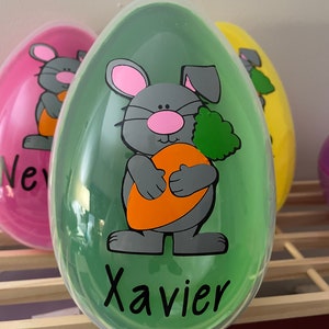 May include: A green plastic Easter egg with a cartoon bunny holding a carrot. The bunny is gray with pink ears and nose. The egg has the name "Xavier" written on it.