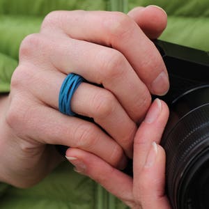 May include: A person's hand wearing a blue silicone ring, holding a black camera with a large lens.