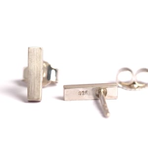 May include: A pair of silver bar stud earrings. The earrings are made of sterling silver and have a brushed finish. The back of one earring shows the marking "925".