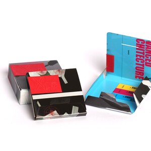 May include: Three boxes with black and white patterns and red accents. The box on the right is open and has a blue interior with the text "ADVANCED ARCHITECTURE" printed on the front.