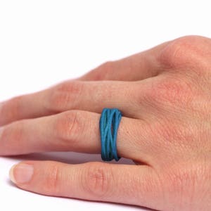 May include: A blue and green woven ring on a person's finger.