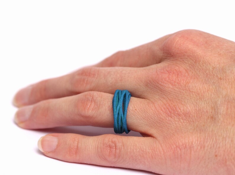 May include: A blue and green woven ring on a person's finger.