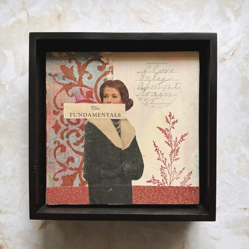 May include: Mixed media artwork in a black frame. The artwork features a vintage image of a woman in a black coat with a cream-colored collar. The text "The Fundamentals" is across the woman's face. A red floral design is on the left.