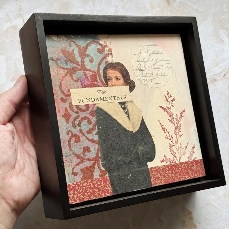 May include: A framed mixed media artwork featuring a vintage image of a woman in a coat with a fur collar. The artwork includes the text "The Fundamentals" and decorative patterns in red, teal, and cream colors.