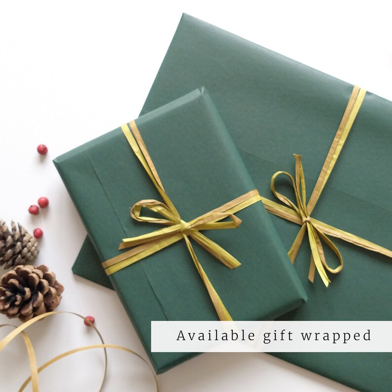 May include: Two green gift boxes wrapped with gold ribbon. The boxes are on a white surface with pine cones and red berries.