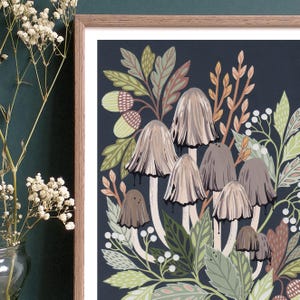 Op de afbeelding: Een ingelijste illustratie van paddenstoelen en bladeren op een donkerblauwe achtergrond. De paddenstoelen zijn lichtbruin van kleur met witte stelen en worden omringd door groene en bruine bladeren. De illustratie is ingelijst in een lichtbruin houten lijst.