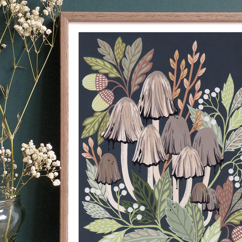 Op de afbeelding: Een ingelijste illustratie van paddenstoelen en bladeren op een donkerblauwe achtergrond. De paddenstoelen zijn lichtbruin van kleur met witte stelen en worden omringd door groene en bruine bladeren. De illustratie is ingelijst in een lichtbruin houten lijst.