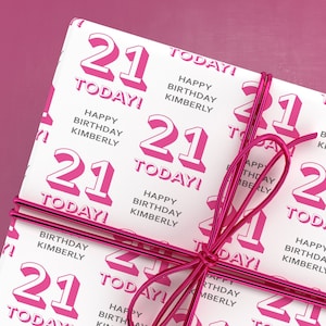 Puede incluir: Papel de regalo blanco con un patr&oacute;n repetido rosa y blanco del n&uacute;mero 21 y el texto "Happy Birthday Kimberly" y "Today!" Una cinta rosa est&aacute; atada alrededor del papel.