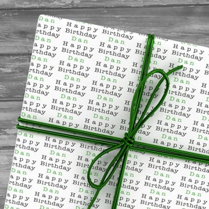 May include: A white gift box wrapped with green ribbon and decorated with the words "Happy Birthday" and "Dan" repeated many times.