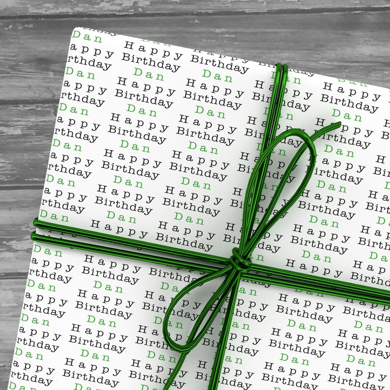May include: A white gift box wrapped with green ribbon and decorated with the words "Happy Birthday" and "Dan" repeated many times.
