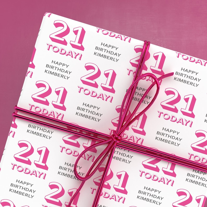 Puede incluir: Papel de regalo blanco con un patr&oacute;n repetido rosa y blanco del n&uacute;mero 21 y el texto "Happy Birthday Kimberly" y "Today!" Una cinta rosa est&aacute; atada alrededor del papel.