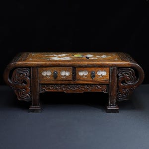 May include: A dark brown wooden chest with two drawers featuring mother-of-pearl inlay. The top surface displays a bird and floral motif, while the drawer fronts show fruit designs. The legs and sides are carved with intricate scrollwork patterns.