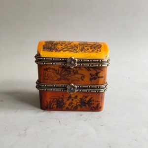 May include: A small, two-tiered wooden box with a hinged lid. The box is decorated with intricate black and white line drawings of birds and flowers. The box has a brass trim and hinges.