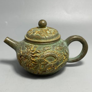 Op de afbeelding: Een klein, groen, bronzen theepot met een drakenontwerp. De theepot heeft een deksel met een knop bovenop en een handvat aan de zijkant.