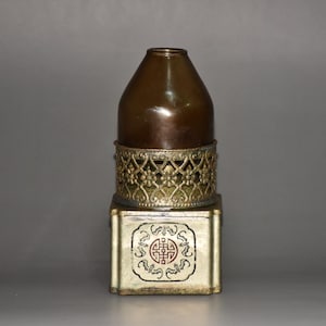 May include: A brown ceramic vase with a gold metal base and a decorative design. The base has a square shape with a floral pattern and a Chinese symbol in the centre.