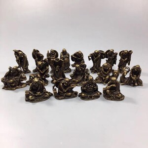 May include: A collection of 18 small, gold-colored, metal figurines of the seven lucky gods of Japanese folklore. The figurines are arranged in a semi-circle on a white surface.