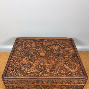 May include: A dark brown wooden box with intricate carvings of dragons and clouds. The box has a hinged lid and a decorative design on the front.