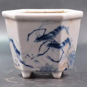 May include: A white porcelain hexagonal planter with blue and white painted shrimp designs. The planter has three small feet.