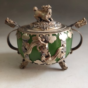 Op de afbeelding: Een kleine groene jade wierookbrander met zilveren accenten. Het deksel heeft een zilveren dierenbeeldje en het lichaam is versierd met zilveren draken. De brander staat op drie zilveren poten.