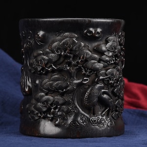 May include: A black carved wooden cup with intricate designs of trees and birds. The cup is made of dark wood and has a smooth, polished finish.