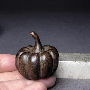 Può includere: Una piccola statuetta di zucca in ceramica di colore marrone scuro. La zucca ha una superficie dettagliata e testurizzata e uno stelo.