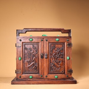May include: A dark wood cabinet with two doors and a carved design. The cabinet has a handle on the top and is decorated with green jade stones.
