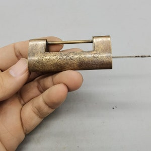 May include: A vintage brass padlock with intricate floral and dragon designs. The padlock has a keyhole and a metal bar that slides through the lock. The padlock is in good condition and has a patina finish.