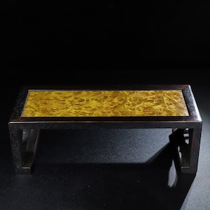 Puede incluir: Una mesa de madera negra con una tapa de madera dorada. La mesa tiene un diseño sencillo con una tapa rectangular y cuatro patas.