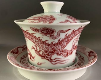 Puede incluir: Un juego de taza y platillo de porcelana blanca con un diseño de dragón rojo. El dragón está representado en un patrón de remolino con nubes y olas. El juego está decorado con un diseño chino tradicional.