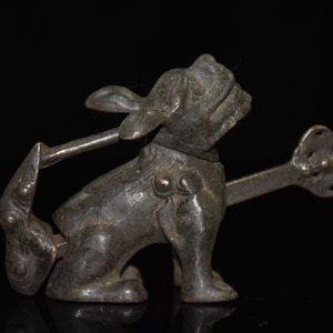 Puede incluir: Una escultura de bronce de una criatura mítica, posiblemente un león o un perro, con un diseño detallado y una cola larga. La escultura está en posición sentada con la cabeza inclinada hacia arriba.
