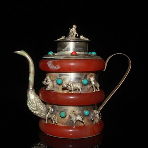 May include: A silver and amber teapot with a lid decorated with turquoise and red stones. The teapot has a silver handle and spout and is decorated with silver animal figures.