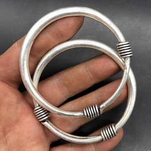Puede incluir: Dos brazaletes de plata con un diseño de alambre retorcido en el cierre. Los brazaletes están apilados uno encima del otro.