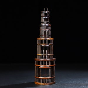 May include: A tall, wooden, tiered birdcage with a dark brown finish. The cage is made of thin, vertical slats and has a square opening in the center of each tier.