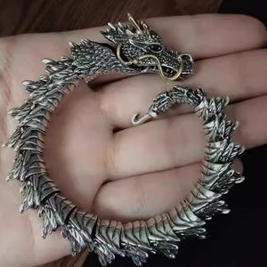 May include: Silver dragon bracelet with a detailed, textured design. The dragon's head is raised and has a gold accent.