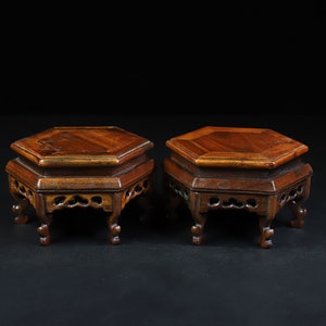 Op de afbeelding: Twee zeshoekige houten display-standaards met ingewikkelde houtsnijwerk op de poten en een donkerbruine afwerking.