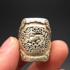 Peut inclure: Une bague en argent avec un motif complexe d'une créature mythique, peut-être un dragon, entourée de motifs floraux.