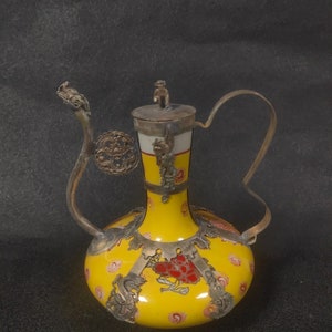 May include: A yellow porcelain teapot with silver accents and floral designs. The teapot has a curved spout and a handle.