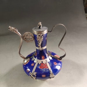 May include: A blue and silver teapot with a dragon spout and floral designs. The teapot has a silver handle and a silver lid with a small figure on top.