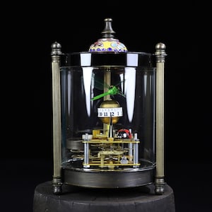 May include: A vintage-style clock with a glass dome, featuring a dragonfly and ladybug design. The clock face has Roman numerals and a gold-colored finish. The clock is encased in a clear glass dome with a brass frame.