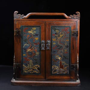May include: A wooden cabinet with two doors, each featuring a colorful dragon design. The cabinet has a handle on top and metal hinges. The doors are closed.