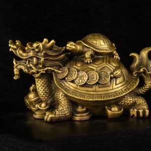 Puede incluir: Una figura de dragón y tortuga de color dorado. El dragón está sobre la espalda de la tortuga, y la tortuga sostiene una cadena de monedas. La figura es un símbolo chino tradicional de buena suerte y prosperidad.