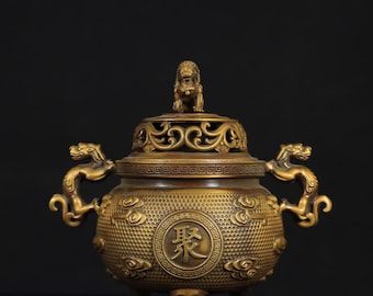 Op de afbeelding: Een bronzen wierookbrander met een deksel met een kleine leeuwenstandbeeld. De brander heeft handvatten in de vorm van een draak en een cirkelvormig ontwerp met Chinese karakters. De behuizing is versierd met wolkenpatronen en staat op drie poten.