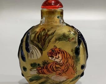 May include: A round glass bottle with a red stopper and a painted image of a tiger in a forest setting. The bottle has a textured, blue and black design.