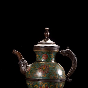 Op de afbeelding: Een metalen theepot met een levendige cloisonné emaille afwerking met ingewikkelde bloemmotieven in tinten turkoois, rood, geel en groen. De theepot heeft een donker metalen deksel met knop, een gebogen tuit en een handvat in de vorm van een draak.