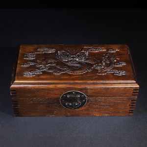 May include: A rectangular wooden box with a carved dragon design on the lid. The box is a warm brown color and has a metal clasp on the front. The dragon is surrounded by clouds.
