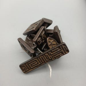 May include: A collection of small, rectangular, dark brown metal stamps with intricate geometric and stylized character designs. The stamps are piled together, with a white string visible.