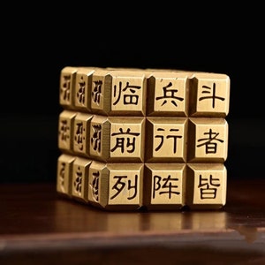 以下が含まれることがあります： 各面に中国語の文字が書かれた金色の立方体。立方体は金属製で、滑らかで磨かれた仕上げになっています。