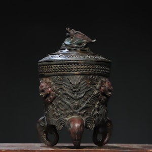 Könnte beinhalten: Ein bronzener Räuchergefäß mit Deckel, mit aufwendigen Reliefs von Drachen und Löwen. Der Brenner hat drei elefantenförmige Beine und einen Drachenaufsatz. Die Farbe ist eine Mischung aus Bronze und Rotbraun.