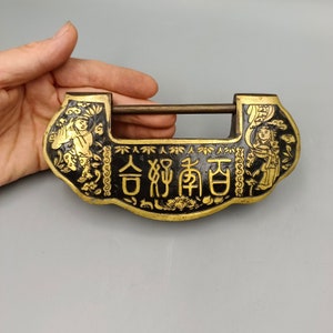 Puede incluir: Un candado chino negro y dorado con diseños intrincados y el texto "合約南宮" en letras doradas.