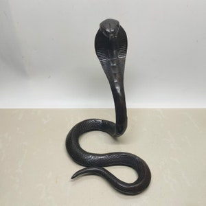 Op de afbeelding: Een zwarte bronzen sculptuur van een cobra met zijn kap omhoog. De sculptuur is gedetailleerd met schubben en een textuur.